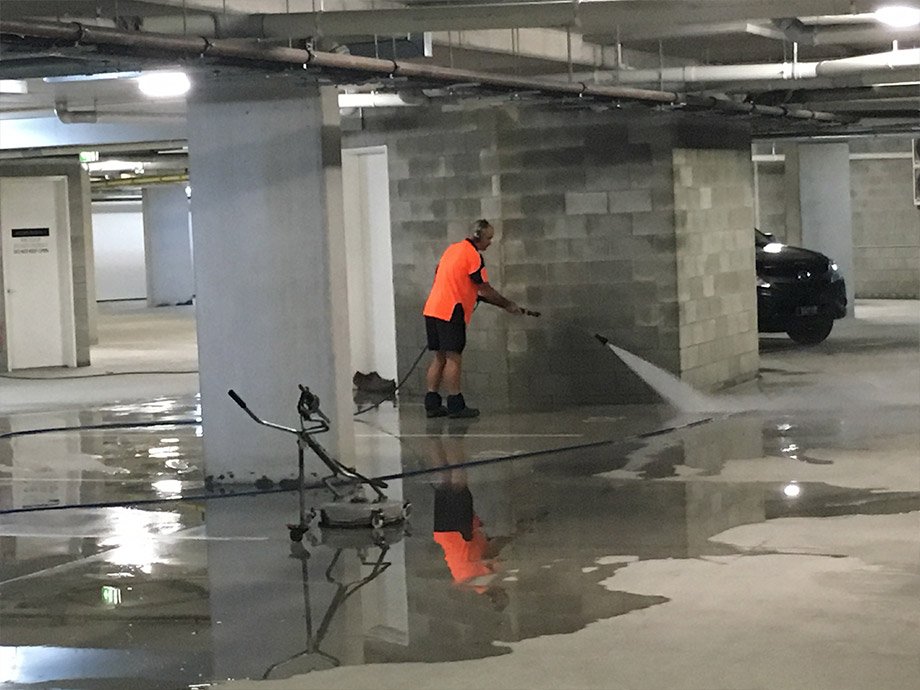 Professional using a pressure washer to clean a car park basement
