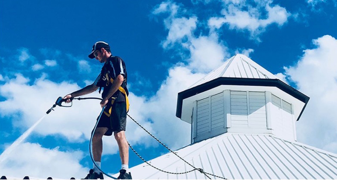 Man standing on a roof professionally cleaning it.