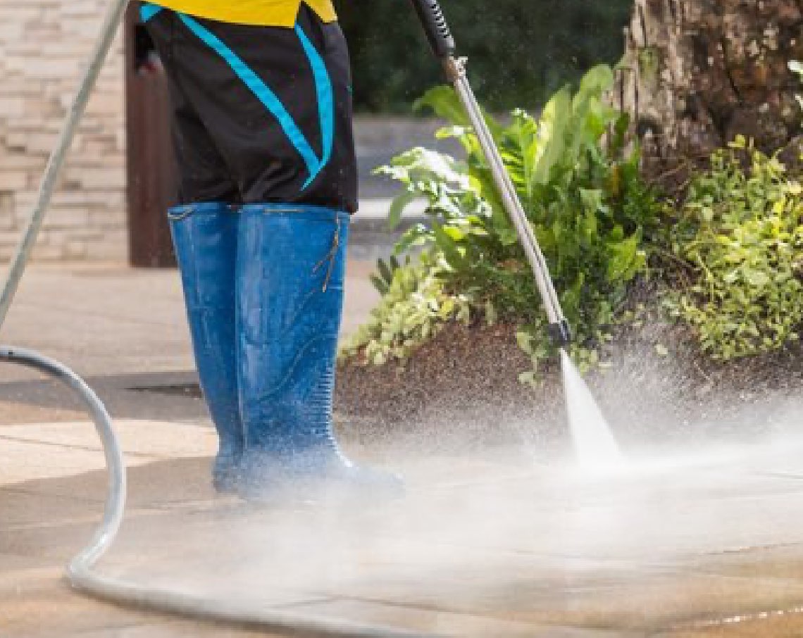 Concrete cleaning in progress, photo of a person wearing boots and pressure washing the ground.